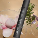 A lifestyle shot of the sleek black Divine Lashes Eyelash Serum next to several natural botanical ingredients.