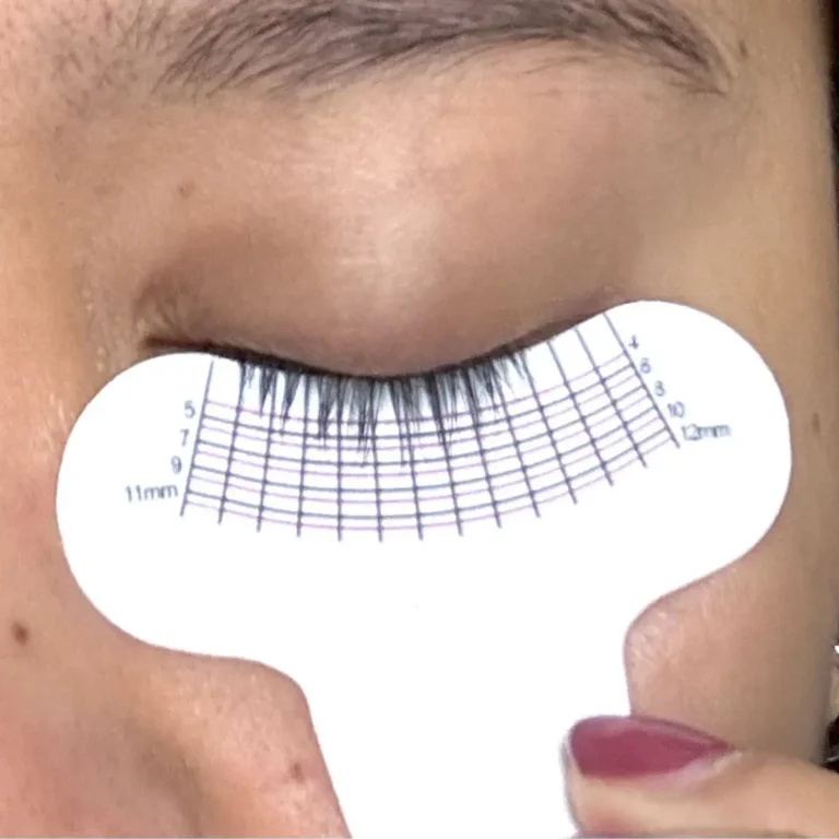 Macro shot of a closed eye showing long, fan-like eyelashes being measured by a white paper lash ruler to demonstrate length from Divine Lashes Enhancing Serum.